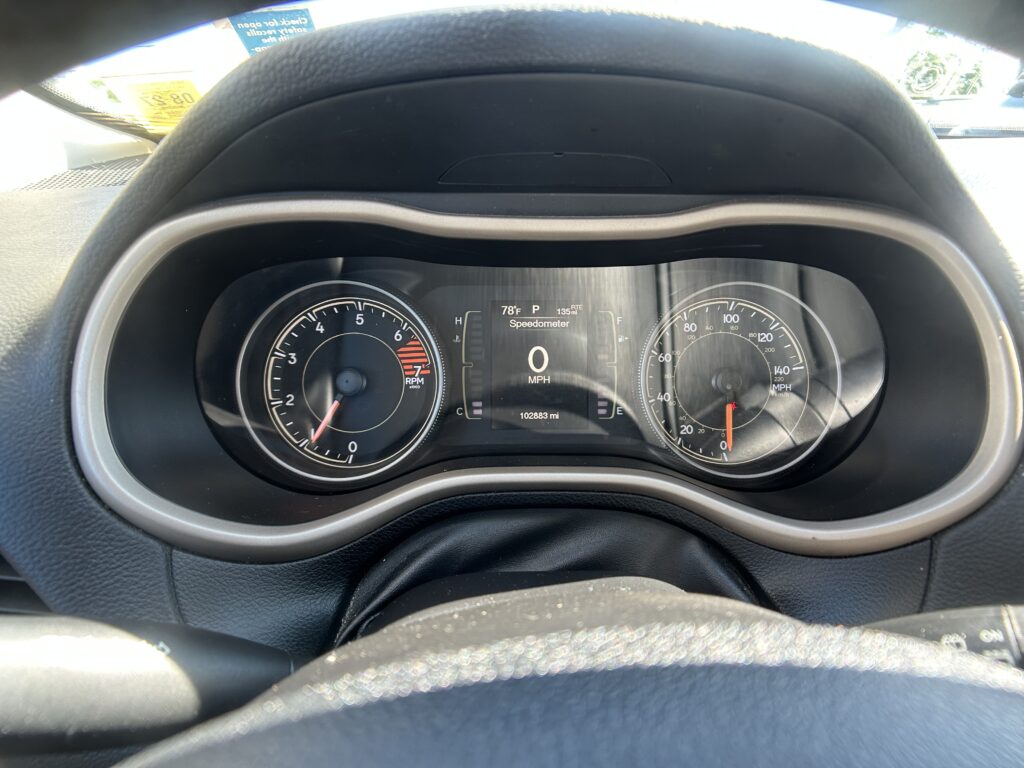 Driver’s-eye view of the dashboard: tachometer and speedometer flanking a central digital display showing 0 mph, 78°F, gear P, and 102,883 miles remaining. The steering wheel is in the foreground.