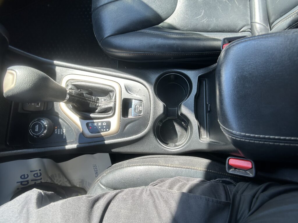 Center console of a car showing the gear shift, cup holders, and black leather seats.