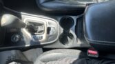 Center console of a car showing the gear shift, cup holders, and black leather seats.