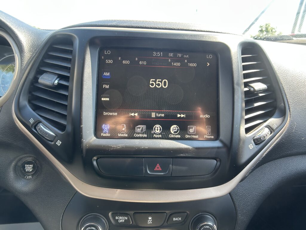 Center touchscreen in car showing FM radio at 550 with surrounding app icons and climate controls visible on the dashboard edge