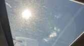 Sunlight shines through a dusty car sunroof, revealing a blue sky outside.