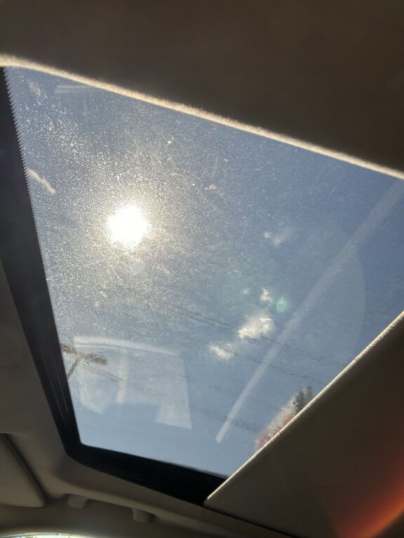 Sunlight shines through a dusty car sunroof, revealing a blue sky outside.