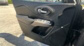 Close-up of a car door interior featuring a silver door handle, black textured trim, and window controls with a speaker grille nearby.
