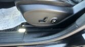 Driver-side car seat with black leather upholstery and power-adjustment controls, including lumbar support lever and seat height knob, on a clean interior panel in daylight.