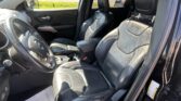 Dark leather car interior with Jeep branding on the front seats, shown from the driver's side, including steering wheel, center console, and outside street view through the windows.
