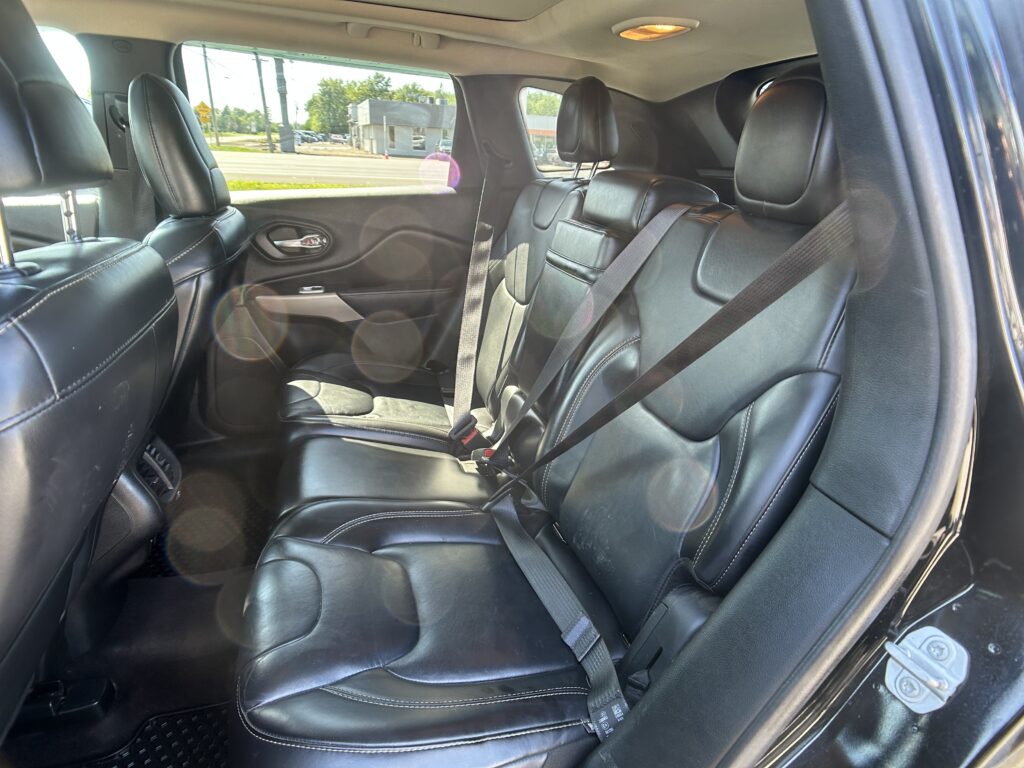 Back seat area of a black leather SUV, showing three headrests and buckled seat belts in sunlight inside the cabin