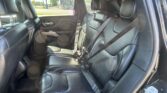 Back seat area of a black leather SUV, showing three headrests and buckled seat belts in sunlight inside the cabin