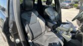 Front row of a black leather SUV interior with driver and passenger seats, center console visible, dealership lot outside the open door.