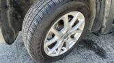 Close-up of a car tire and alloy wheel with dirt-splattered wheel well, resting on a paved surface.