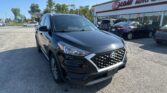 Front corner of a black Hyundai SUV parked in a dealership lot with a white building and 'E-Z LOAN AUTO SALES' sign in the background.