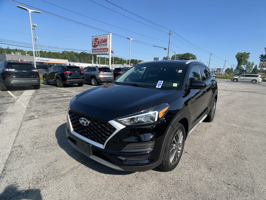 Front‑facing view of a black Hyundai SUV in a car dealership lot, with multiple vehicles and an EZ LOAN Auto Sales sign in the background.