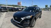 Front‑facing view of a black Hyundai SUV in a car dealership lot, with multiple vehicles and an EZ LOAN Auto Sales sign in the background.