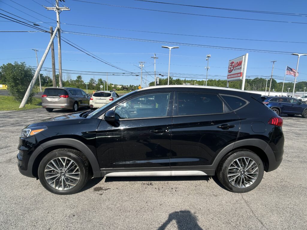 Black SUV in a dealership lot with utility poles and power lines overhead, and a red-and-white EZ Loan Auto Sales sign in the background—clear sky.