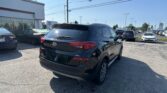 Black Hyundai SUV seen from the rear in a sunny car dealership lot, with a white showroom building and Toyota signs in the background.
