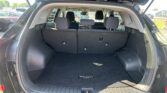 Open rear hatch of a dark SUV showing a spacious cargo area with the back seats upright and a Tucson-branded floor mat visible in the floor.