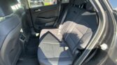 Rear passenger seats of a dark interior car with seat belts and headrests; outside parking lot visible through the window.