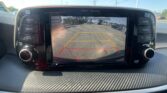 Rearview camera display on the car’s dashboard showing parking guidelines and the message 'Check surroundings for your safety.' in a dealership lot.