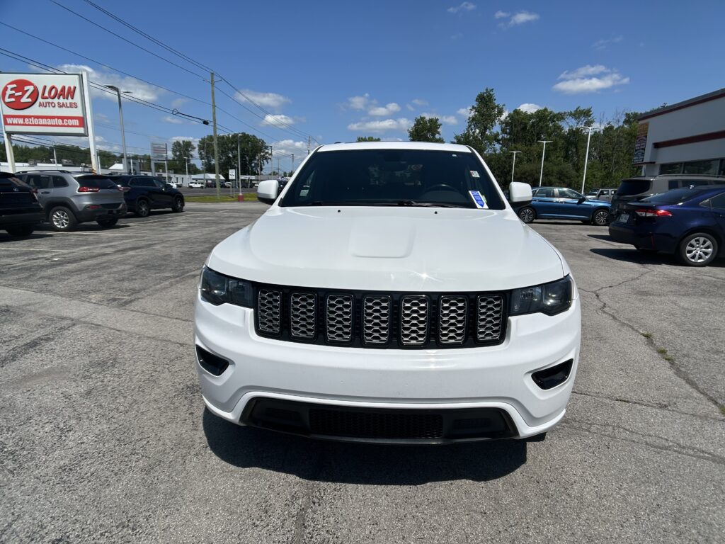 Front view of a white SUV with a black grille, parked in a dealership lot under a blue sky, with an E-Z LOAN sign in the background.