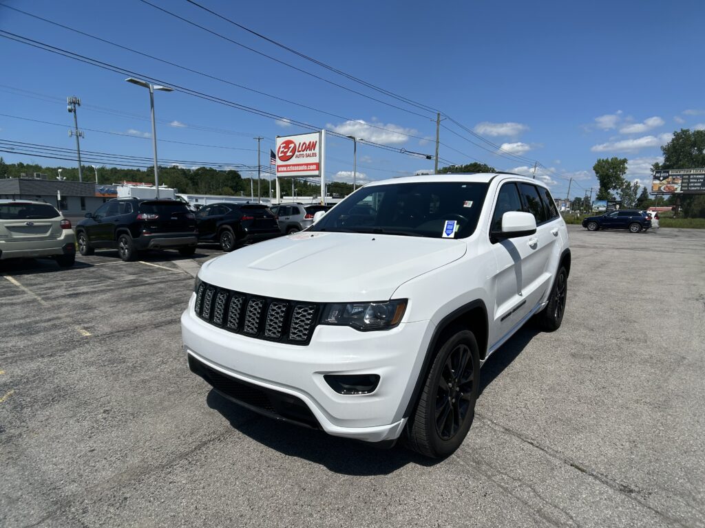 Front-right view of a white SUV in a car dealership lot with other vehicles and an EZ LOAN Auto Sales sign in the background on a sunny day.