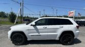 White SUV (Jeep Grand Cherokee) in a parking lot with utility poles and multiple power lines overhead; dealership sign and American flag visible in the background