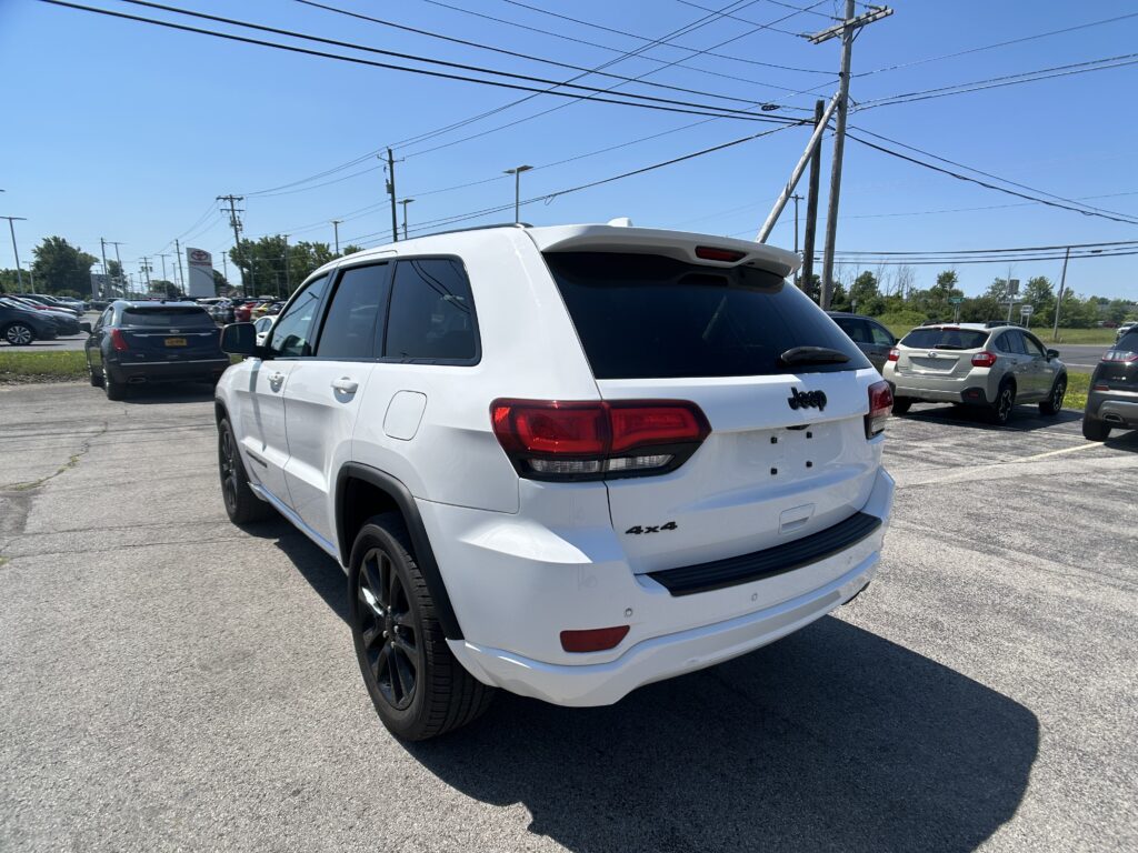 White Jeep SUV seen from the rear three-quarter angle in a sunny parking lot, with other cars nearby and a '4x4' badge visible on the tailgate.