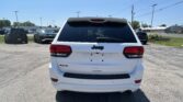 Rear view of a white Jeep SUV in a parking lot, with other cars and power lines against a clear blue sky.