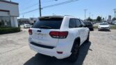 White Jeep SUV shown from the rear side in a dealership lot with many cars and a Toyota dealership building in the background.