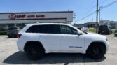 White Jeep Grand Cherokee SUV in a parking lot in front of an E-Z Loan Auto Sales building with a clear blue sky behind it.