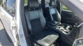 Open car door showing black leather front seats and center console in a light-colored vehicle exterior, bright daylight outside.