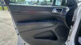 Interior of a car door panel with the window down and chrome door handle, view of the side mirror; a parking lot with multiple cars outside visible through the window.