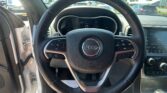 Driver’s view inside a Jeep: steering wheel with logo, dashboard, and the open driver’s door; a parking lot is visible outside the windshield.