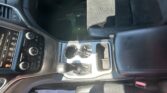 Interior of a car showing the center console with gear shifter, cupholders, and a touchscreen control panel nearby on the left side of the image.