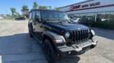 Black Jeep Wrangler in a dealership lot with EZ Loan Auto Sales sign on the building under a clear blue sky.