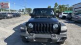 Front view of a black Jeep Wrangler parked in a dealership lot, with an EZ Loan Auto Sales sign visible on the left and other cars surrounding the lot under a clear blue sky.