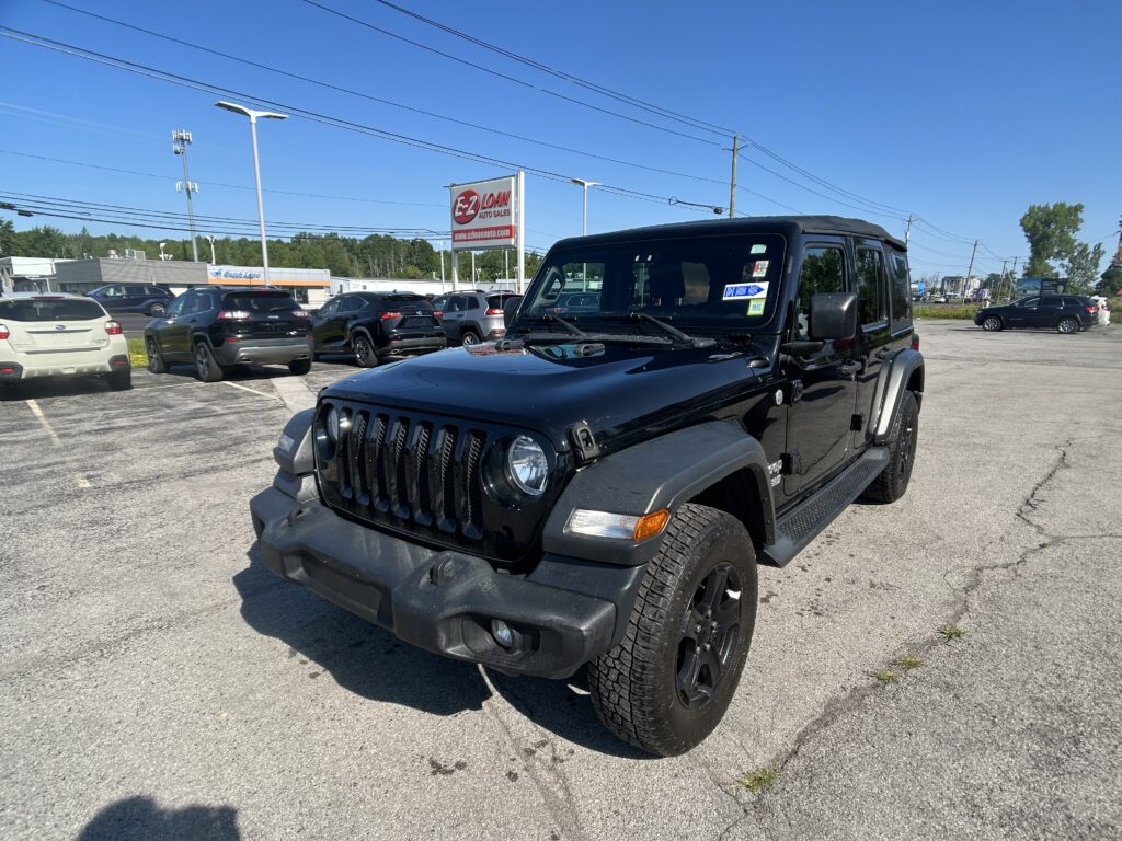 Black Jeep Wrangler in a dealership lot with several other cars and an EZ Loan Auto Sales sign in the background under a blue sky.