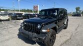 Black Jeep Wrangler in a dealership lot with several other cars and an EZ Loan Auto Sales sign in the background under a blue sky.