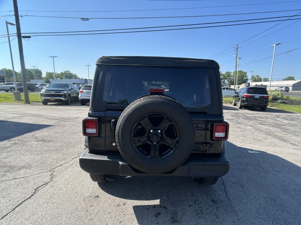 Rear view of a black SUV with a spare tire mounted on the tailgate in a parking lot, other cars and power lines in the background.