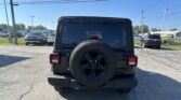 Rear view of a black SUV with a spare tire mounted on the tailgate in a parking lot, other cars and power lines in the background.