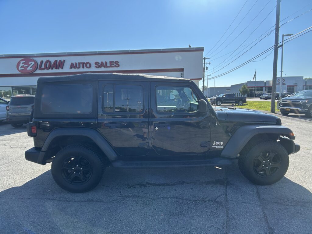 Black Jeep Wrangler parked in a dealership lot with the E-Z Loan Auto Sales sign and other vehicles in the background, under a clear blue sky.