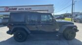 Black Jeep Wrangler parked in a dealership lot with the E-Z Loan Auto Sales sign and other vehicles in the background, under a clear blue sky.