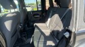 Back seat area of a black SUV with three head restraints and visible seat belts, viewed from the open rear door; outside cars in a parking lot visible through windows.