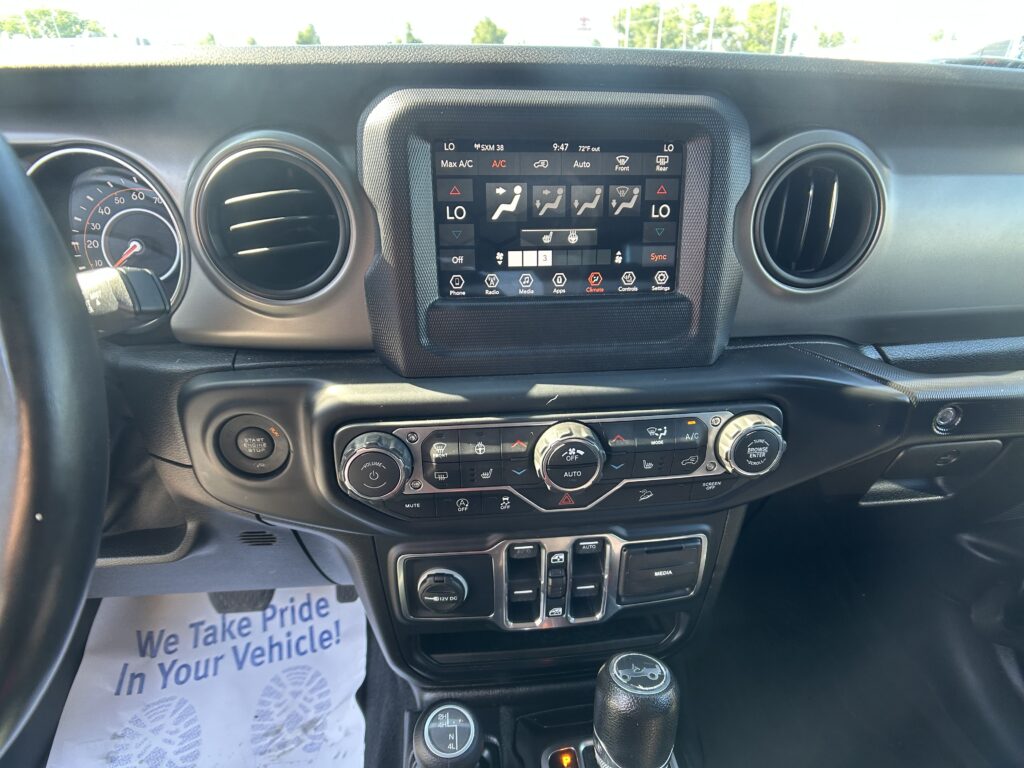 Dashboard interior of a vehicle with a center touchscreen climate/display panel and gear shifter, plus papers on the floor.