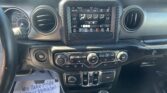 Dashboard interior of a vehicle with a center touchscreen climate/display panel and gear shifter, plus papers on the floor.