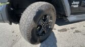 Close-up of a rugged tire and black alloy wheel on a Jeep Wrangler, with the wheel well and fender visible.