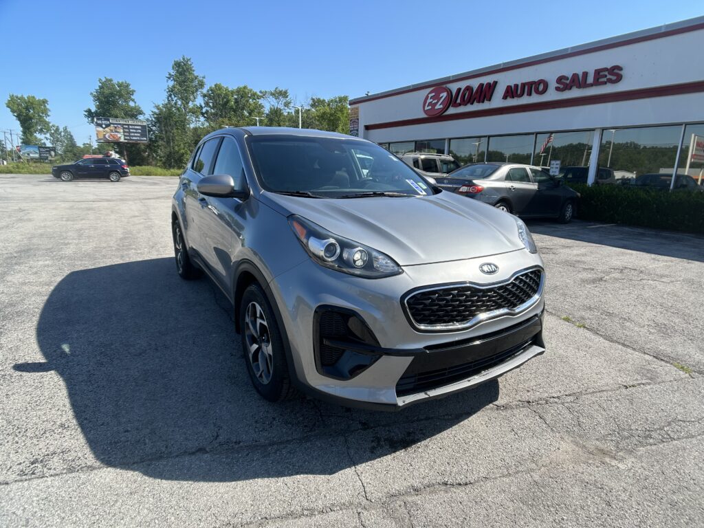 Silver Kia SUV in the foreground at a car dealership lot with EZ Loan Auto Sales building in the background