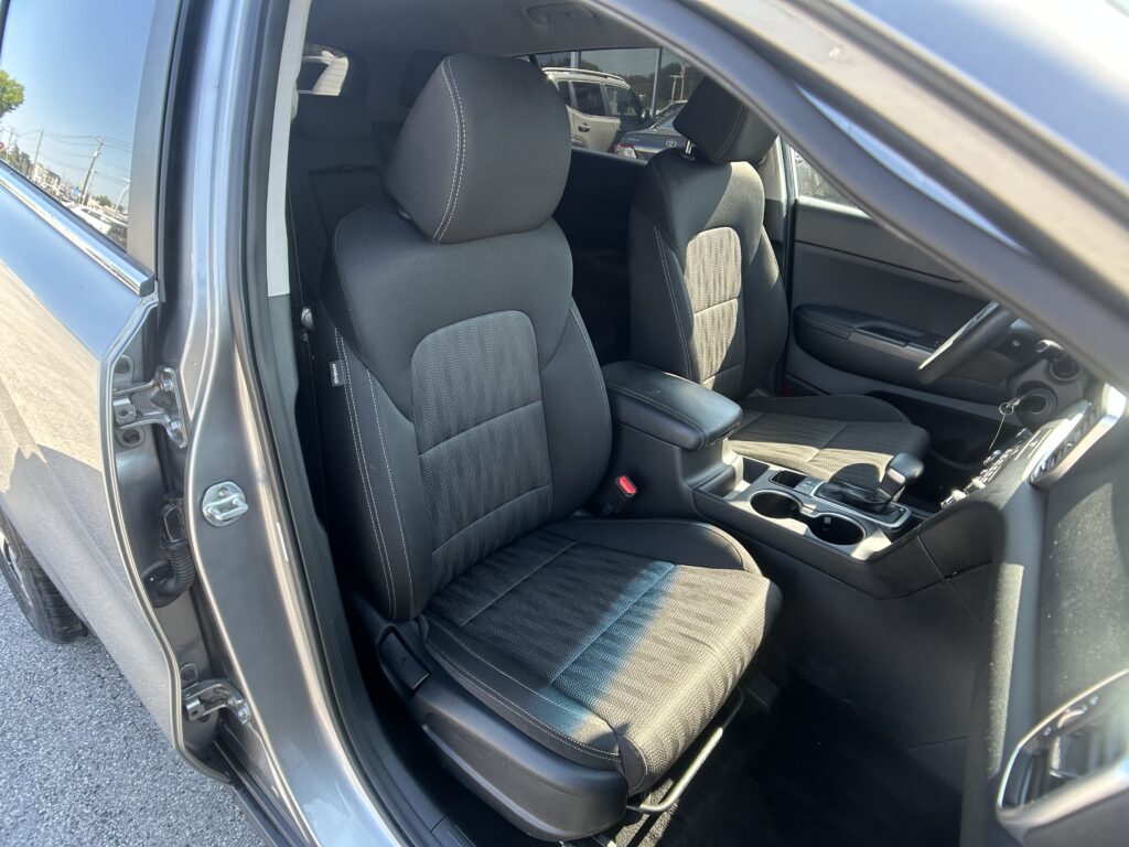 Interior view of a car showing two front seats with black fabric and white stitching, center console visible