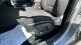 Front interior of a car: central console with gear shifter, black fabric seats, and sunlit passenger side door frame visible. A protective paper mat lies on the floor.