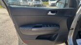 Interior of a car door with power window controls and door handle, view of outdoor car lot through the window