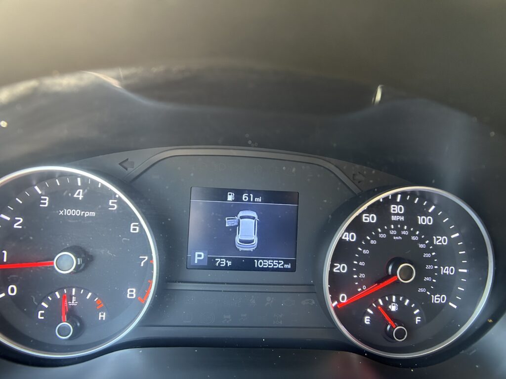 Dashboard view of a car instrument cluster: tachometer on left, speedometer on right, center display shows vehicle icon, parked (P), 73°F, 103,552 miles.