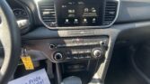 Car dashboard interior with a touchscreen infotainment system displaying 96.9 FM, surrounding controls, and a steering wheel on the left; papers on the passenger side say 'We Take Pride in Your Vehicle'.